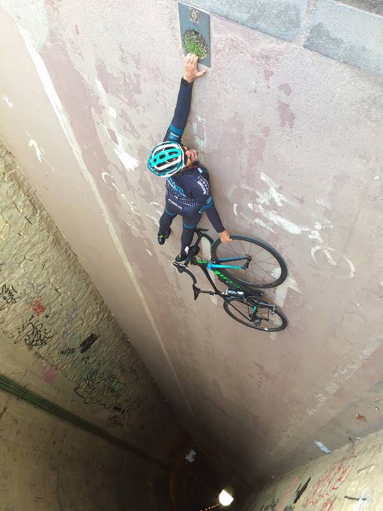 Man looks like he is hanging on to a wall with his bike, but it is just the camera angle of an underpass tunnel