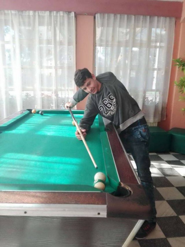 kid playing pool trick shot with one arm bent behind his body
