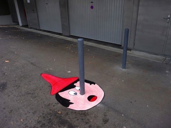 Pole sticking out of the ground has street artwork drawn around it like Pinocchio and his nose.