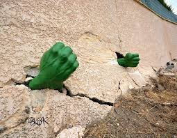 Cracks in a building wall that has green fists added to it to make it look like an awakening Hulk is inside.