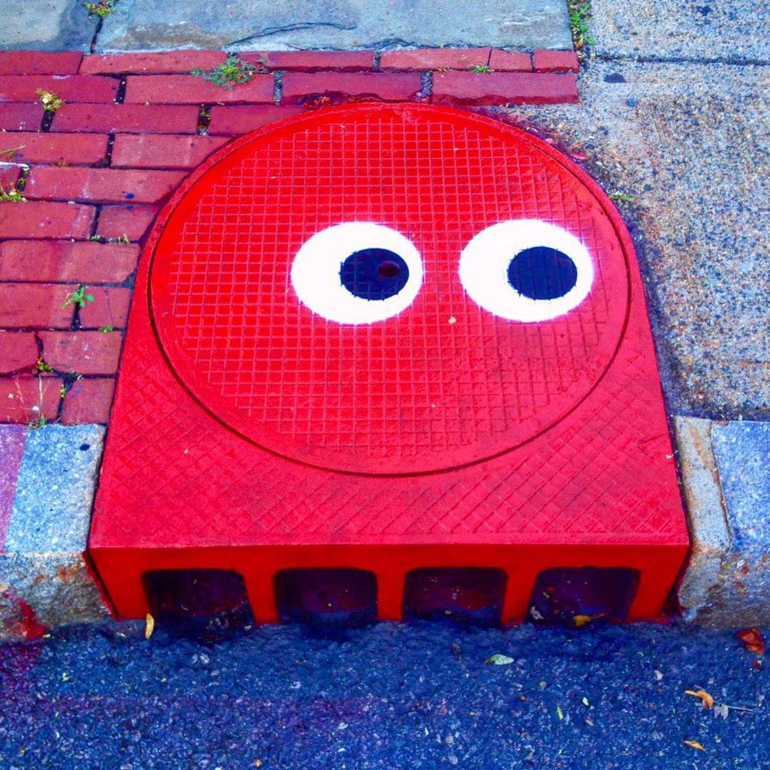 Sewer manhole cover that has been painted to look like a cute red squid with googly eyes