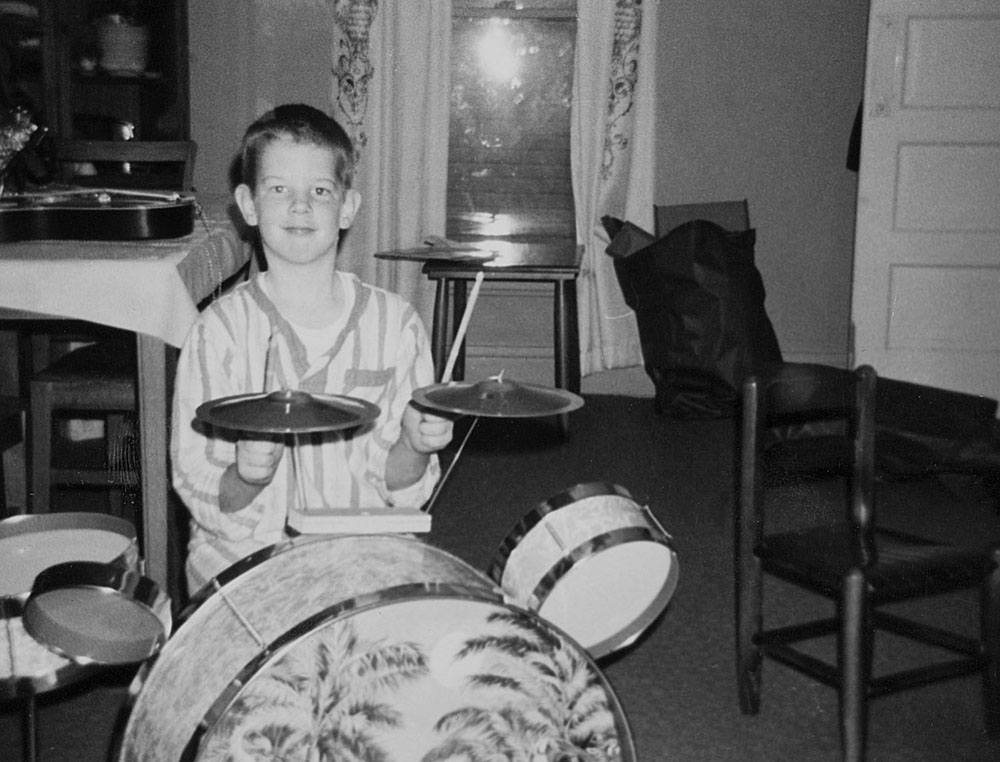 Young boy in pajamas play the drums in his living room.