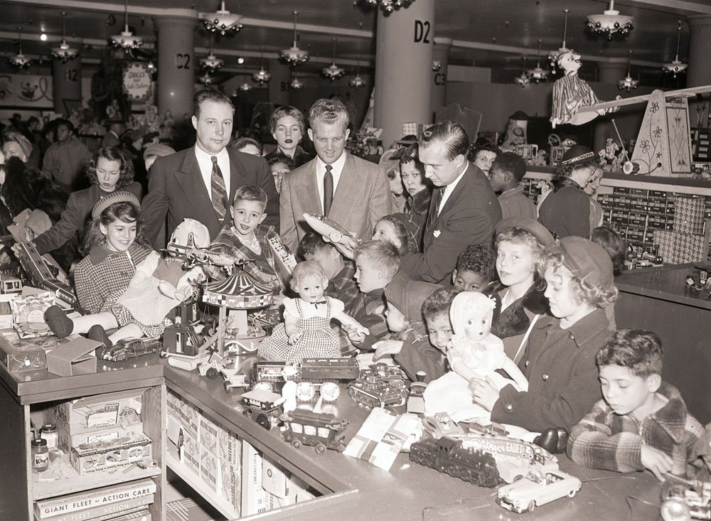 12/9/1952-New York: Nearly 500 orphans from the metropolitan area found “daddies for a day” in members of the Young Men’s Board of Trade who conducted them on a tour of Gimbel’s toy department and provided each with a $5 bill to use to buy anything they wanted. Photo shows some of the kids touching and appreciating a life size doll on the counter.