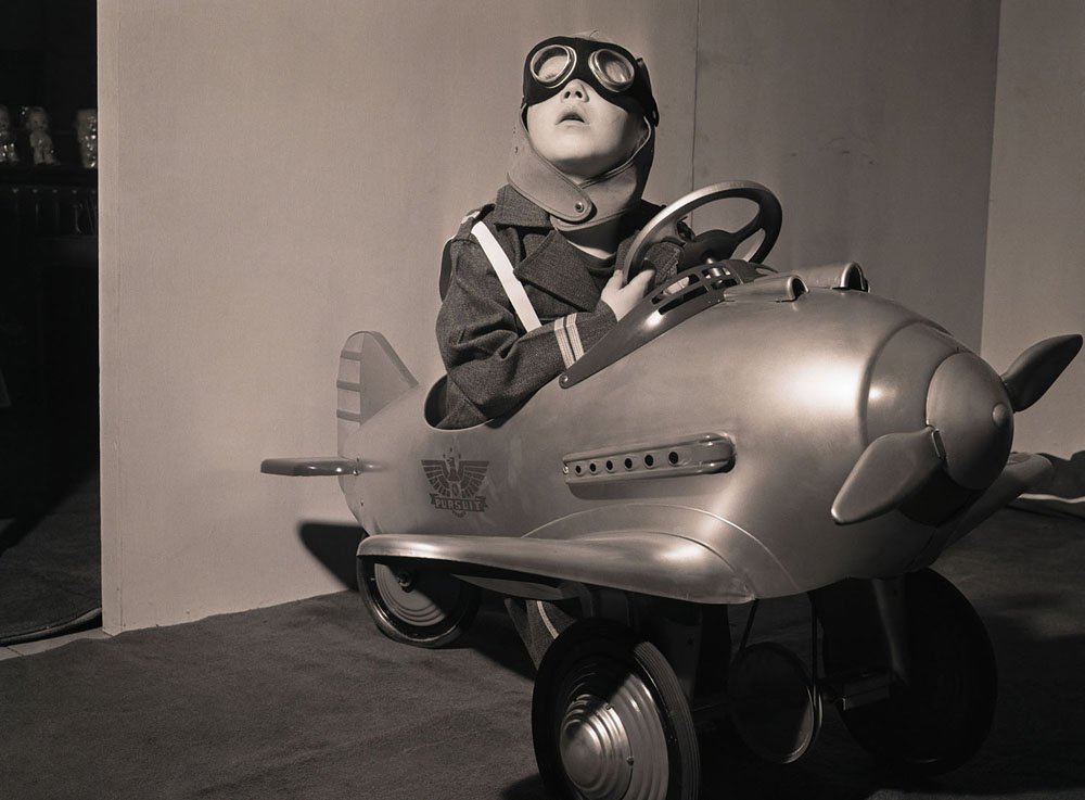 Little Craig Smith looks around for enemy planes as he daydreams in a toy fighter plane. This model fighter plane reflects the spirit of wartime America, a country which may experience shortages in toys at Christmastime due to the need to support the war effort.