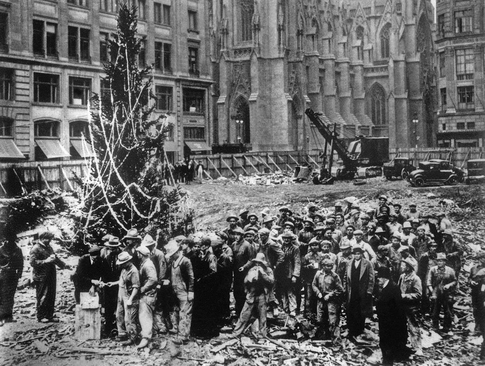 Construction workers line up for pay beside the first Rockefeller Center Christmas tree in New York in 1931. The Christmas tree went on to become an annual tradition and a New York landmark. St. Patrick’s Cathedral is visible in the background on Fifth Avenue.