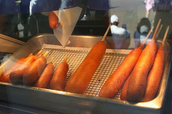 Corn Dogs
There’s a lot of people vying for credit for the invention of the Corn Dog. According to some sources, German immigrants arriving in Texas, looking to sell their meat products, found that battering their sausages in a mixture of cornmeal, self-rising flour, eggs and various spices, deep frying it and impaling it on a stick made them more popular.
On the other hand, there’s also some sausage and hot dog shops in California, Illinois and Minnesota that lay claim to putting their hotdogs in batter and serving them on a stick.
Either way, whoever invented them, they’re awesome with some Dijon mustard.