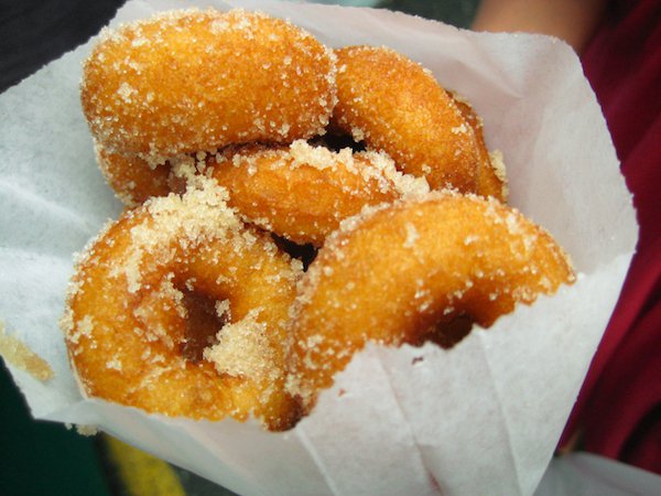 Mini Donuts
The origins of who invented the donut are varied, as there are multiple influences all over the world. The most commonly accepted history is that dutch settlers brought over little mini dough cakes that they filled with cremes and preserves, and fried. Keep in mind, these were whole cakes. Apparently a sea captain, tired of how greasy they were and occasionally finding an uncooked centre, started punching a hole in the middle. There’s also an anecdote that claims he put a hole so he could rest the donut on a peg on his ships wheel, for ease of eating.
When it comes to the mini donut, apparently during the Spanish-American war in the 1890’s, to better ration the food, mini donuts were distributed to the soldiers.
From there, machines were invented to make the mini donuts quickly and this popular treat became synonymous with carnivals, especially when dusted with cinnamon and sugar.