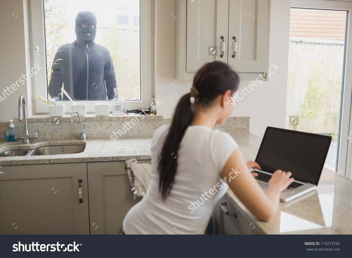 Woman on a computer that has a screen turned off and a man with face mask in the window