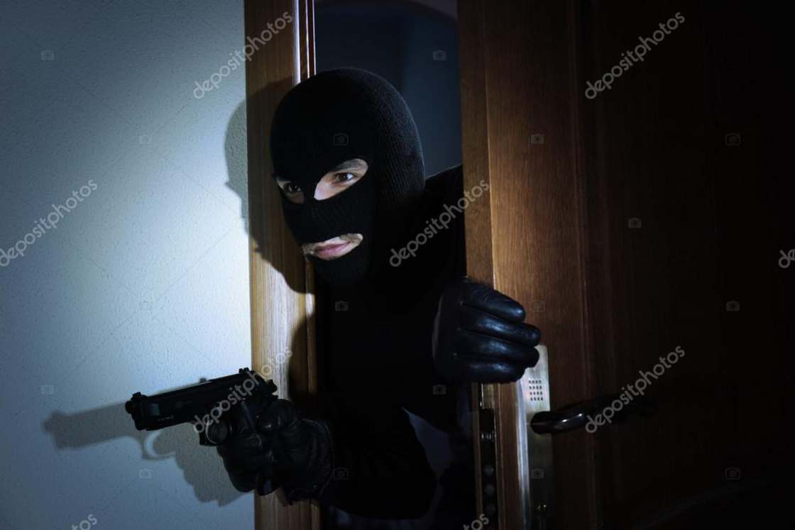 WTF stock image of a kid wearing balaclava face mask and holding a gun at night.