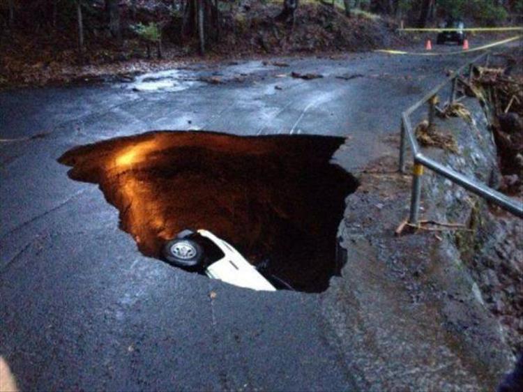 random picture of a sink hole in the middle of the road that swallowed a pickup truck