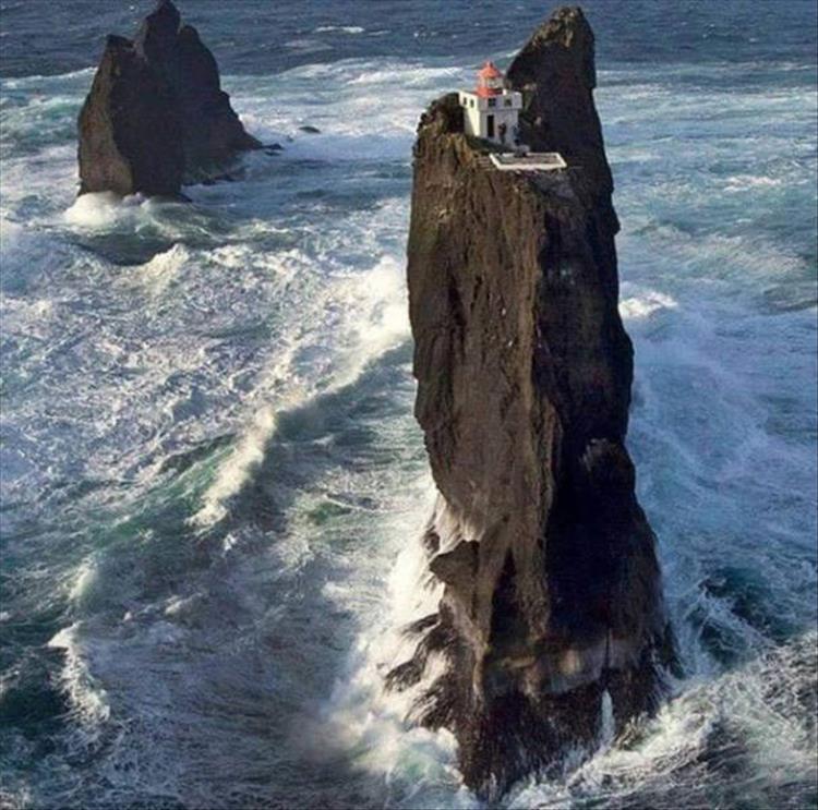 random picture of rock stick out of the ocean with a house on top of it