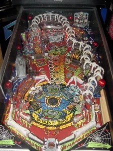 Scared Stiff (1996)
Scared Stiff features the well-known horror show mistress, Elvira from Elvira, Mistress of the Dark. It is the follow-up game to Elvira and the Party Monsters. This pinball machine has a B-movie horror theme, and the player must go through six tales of terror to level up the Stiff-O-Meter. One of the coolest features of this game is the player controlled spinning spider on the backbox.