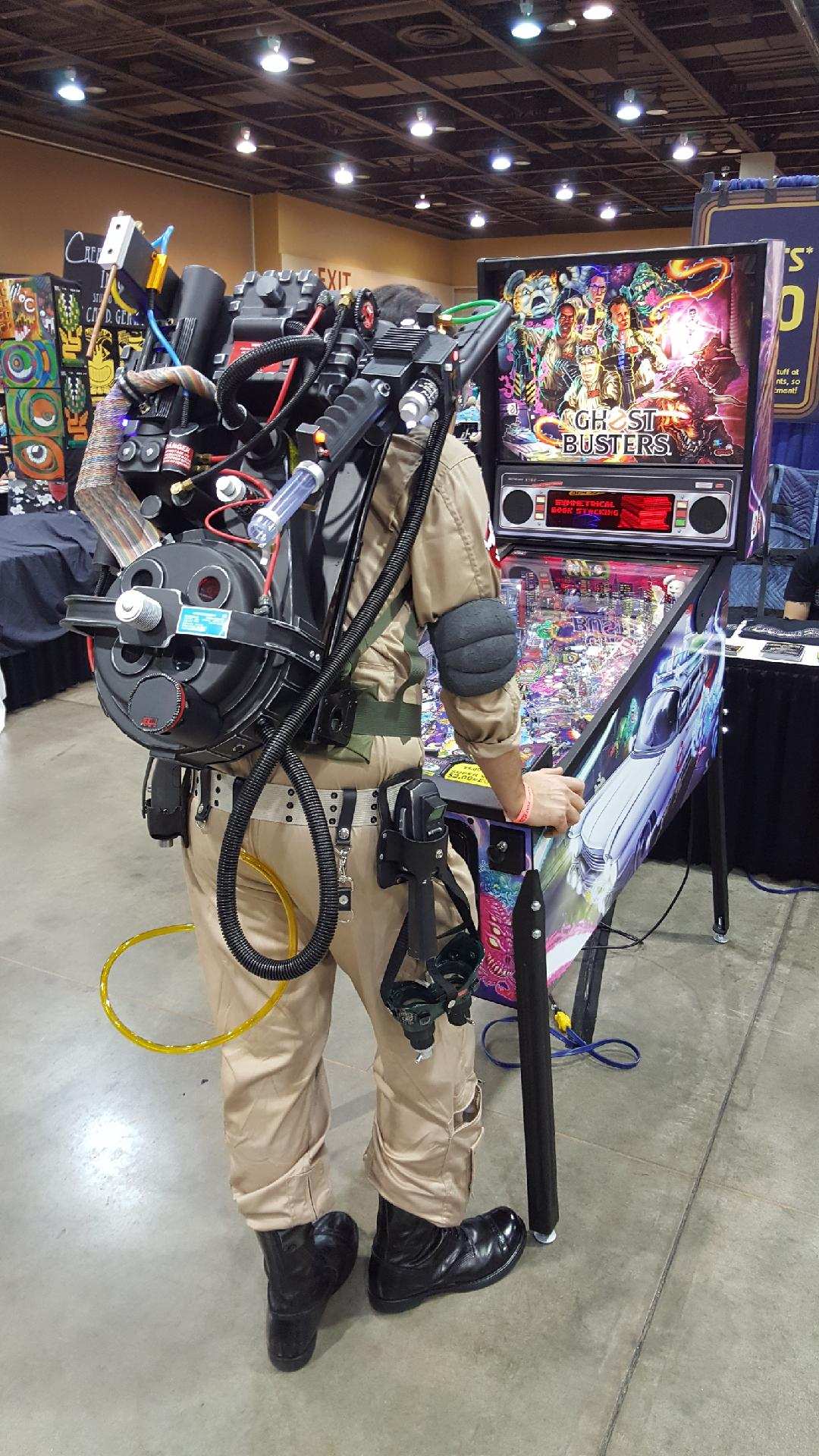 Man dressed in full costume of Ghostbusters casually playing a pinball machine about ghostbusters.