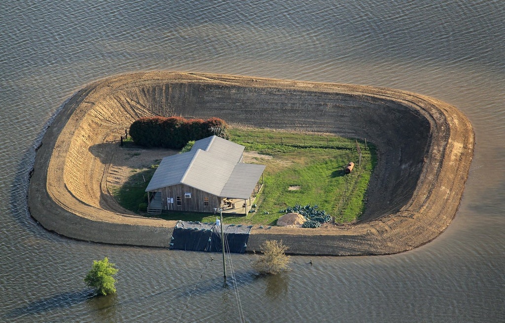 small ranch with large berm around the house to protect it from the flood surrounding it