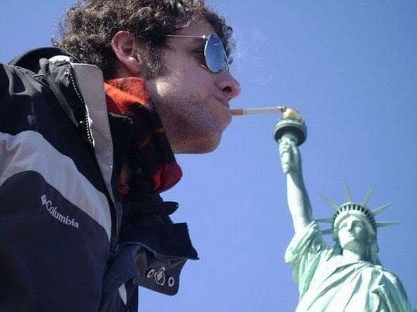 man with sunglasses looks like he is having his cigarette lite by the torch of the statue of liberty
