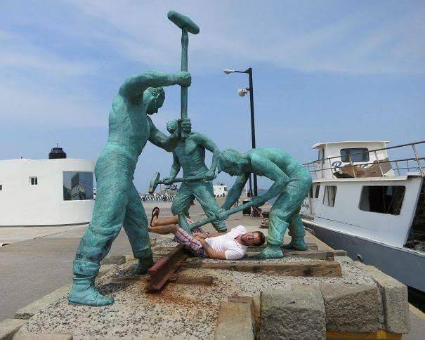 man posing as if he is being beaten by green marble statues