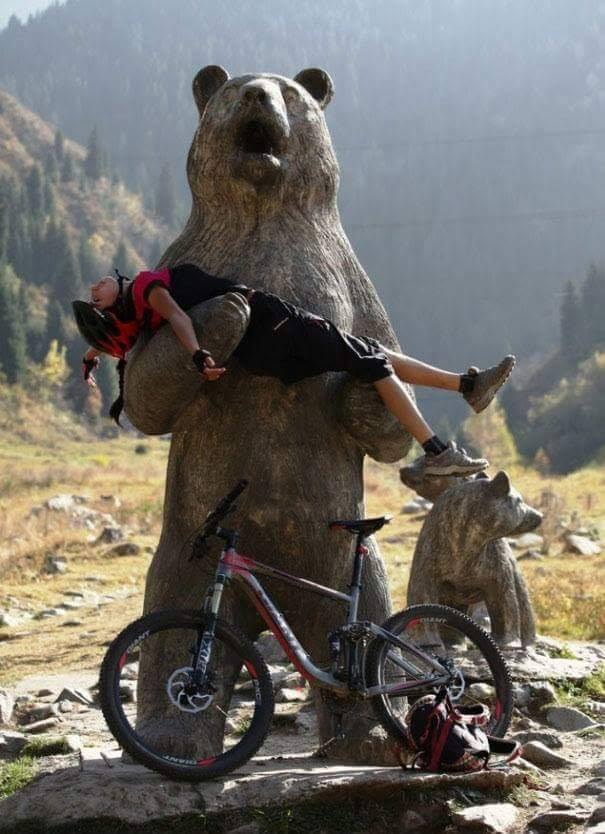 biker posing as if being carried by statue of a bear