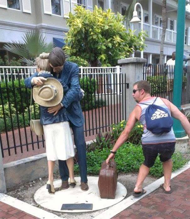 man posting with statue of couple hugging as if he is about to seal his briefcase