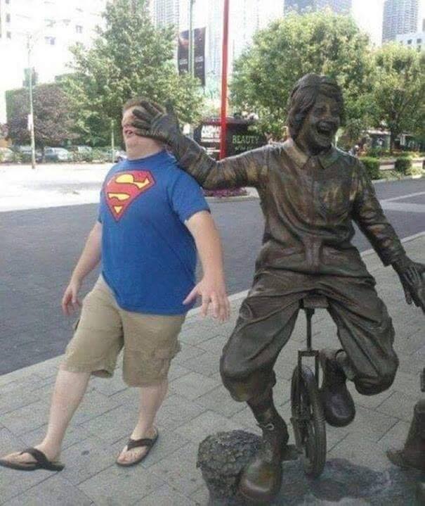 man with superman t-shirt getting knocked in the face by unicycle statue