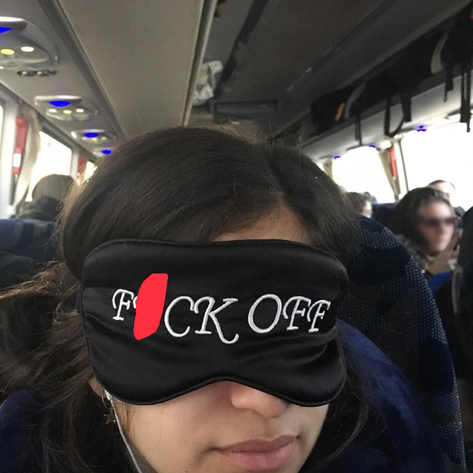 pic of a woman on public transport wearing a sleeping mask that says 'fuck you'