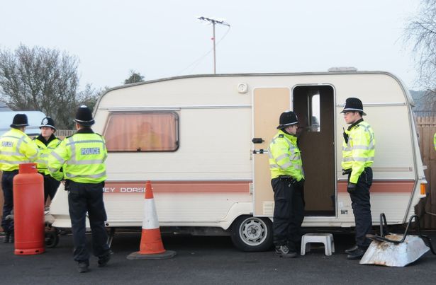 Police outside a caravan occupied by one of the workers at a travellers site