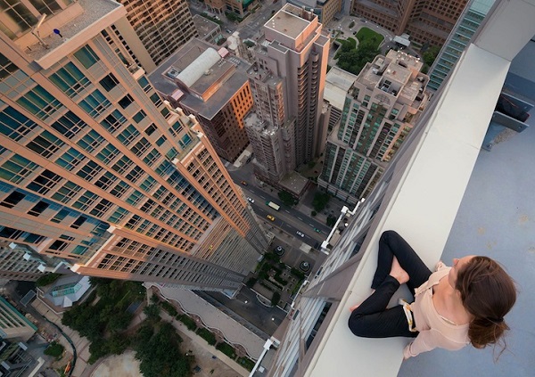 Overhead photograph of a woman sitting on the edge of a very tall building