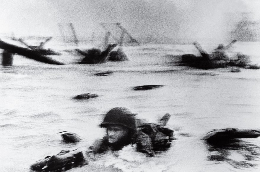 D-Day, Robert Capa, 1944

It was the invasion to save civilization, and LIFE’s Robert Capa was there, the only still photographer to wade with the 34,250 troops onto Omaha Beach during the D-Day landing. His photographs—infused with jarring movement from the center of that brutal assault—gave the public an American soldier’s view of the dangers of war. The soldier in this case was Private First Class Huston Riley, who after the Nazis shelled his landing craft jumped into water so deep that he had to walk along the bottom until he could hold his breath no more. When he activated his Navy M-26 belt life preservers and floated to the surface, Riley became a target for the guns and artillery shells mowing down his comrades. Struck several times, the 22-year-old soldier took about half an hour to reach the Normandy shore. Capa took this photo of him in the surf and then with the assistance of a sergeant helped Riley, who later recalled thinking, “What the hell is this guy doing here? I can’t believe it. Here’s a cameraman on the shore.” Capa spent an hour and a half under fire as men around him died. A courier then transported his four rolls of film to LIFE’s London offices, and the magazine’s general manager stopped the presses to get them into the June 19 issue. Most of the film, though, showed no images after processing, and only some frames survived. The remaining images have a grainy, blurry look that gives them the frenetic feel of action, a quality that has come to define our collective memory of that epic clash.