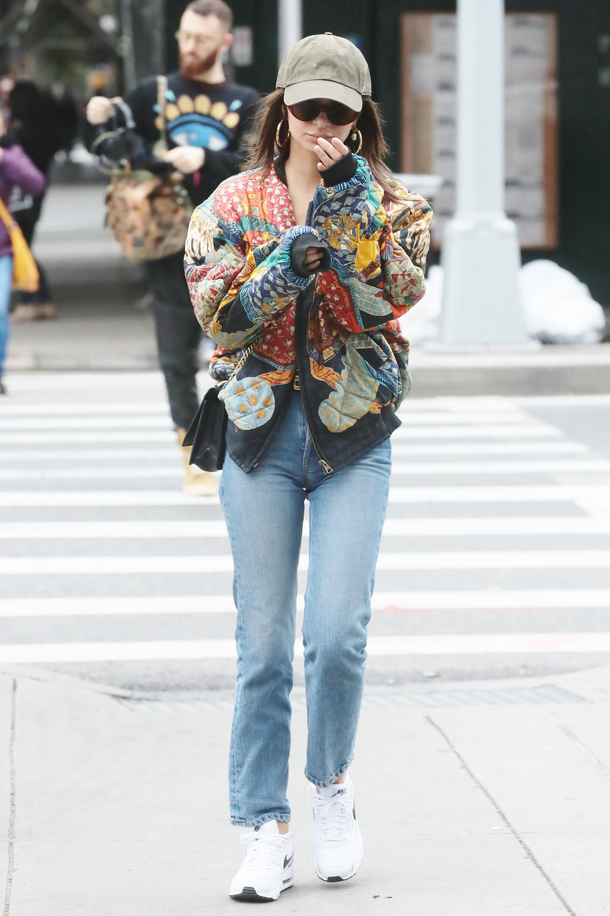 Model Emily Ratajkowski wearing jeans and a colorful top walking down a sidewalk in 2019. 