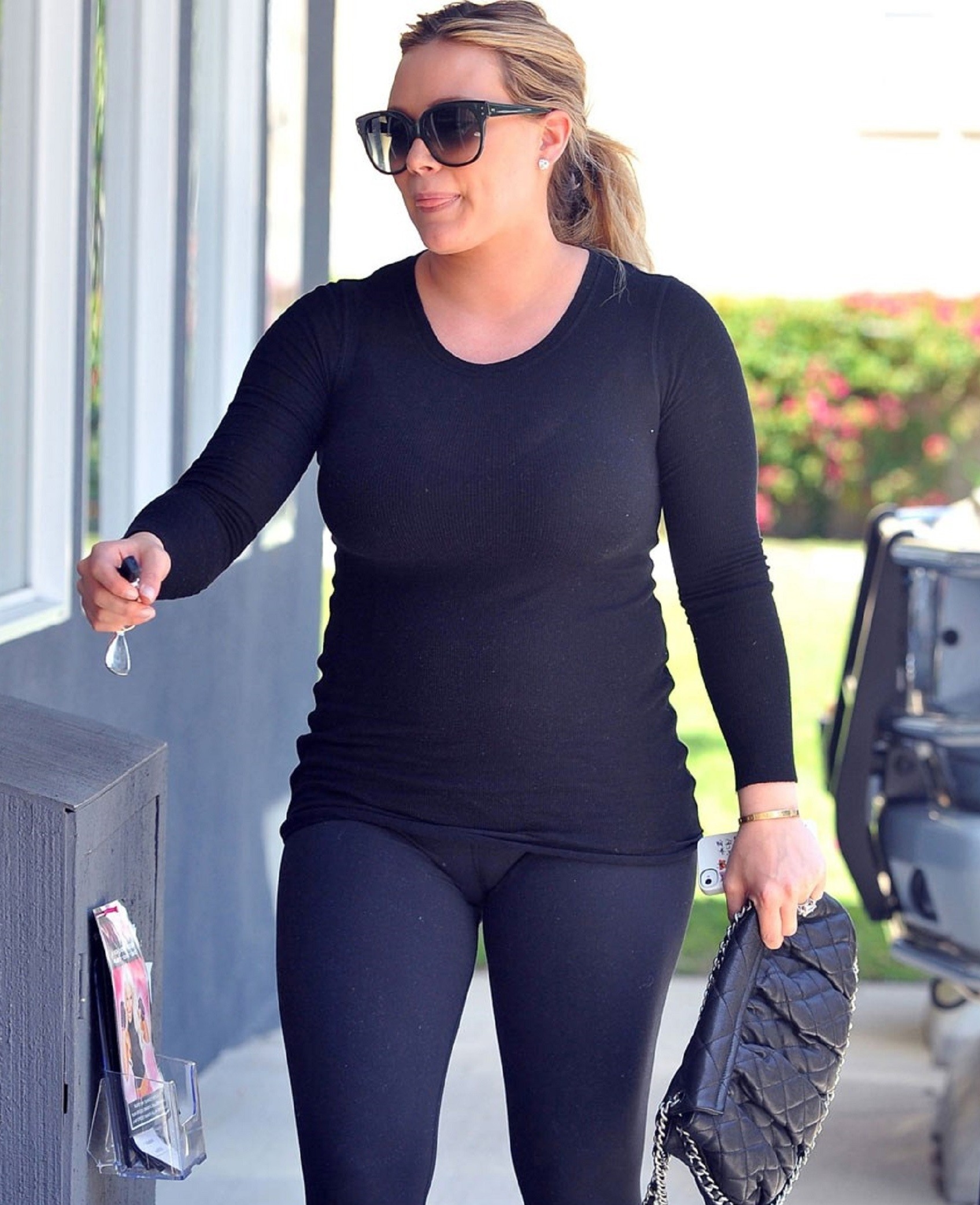 Hillary Duff wearing a tight black top and black yoga pants with visible ca...