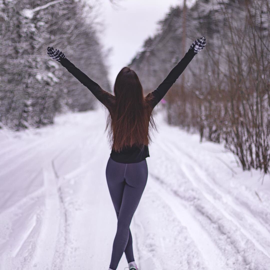 Beautiful girl walking down a snowy road with her hands in the air wearing yoga pants.