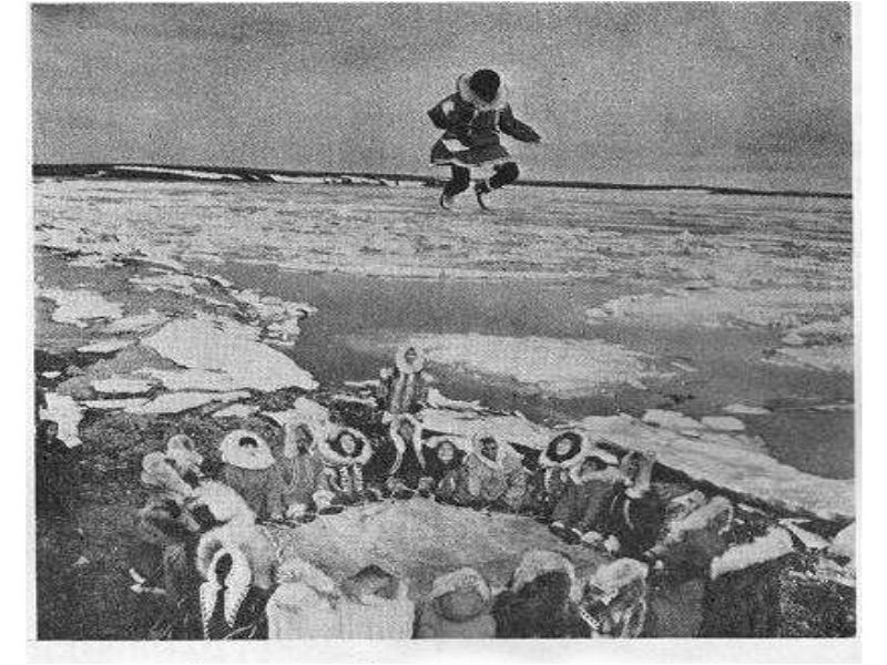 An odd image of a group of people dressed like Eskimos looking up at a flying person.