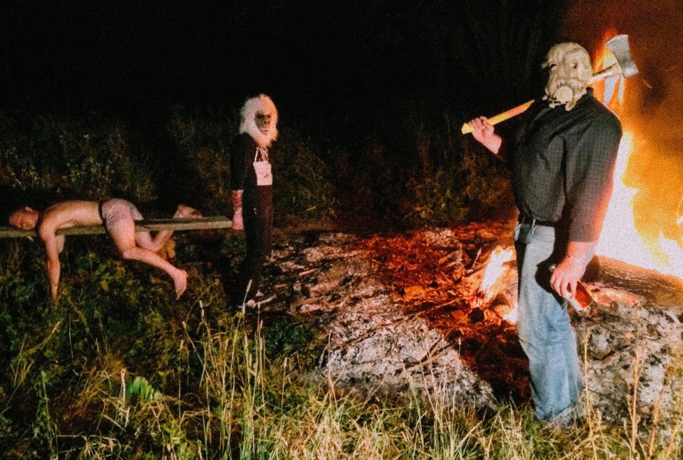 A disturbing photo of a man passed out by a bonfire with people dressed in weird costumes nearby.