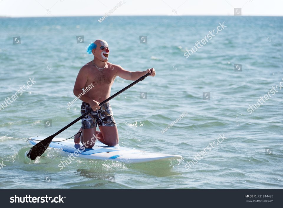 A weird stock photo of a clown on a paddle board. 