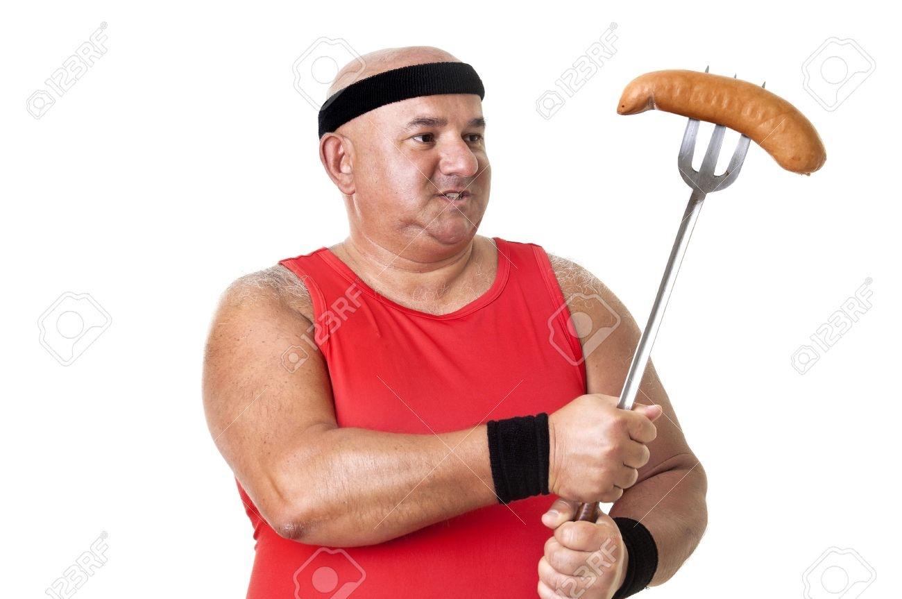 A WTF stock photo of a man in a red shirt holding a sausage on a large fork. 
