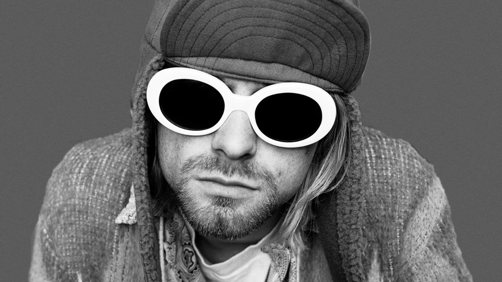A photo of Kurt Cobain with white glasses and a hat with the lip up