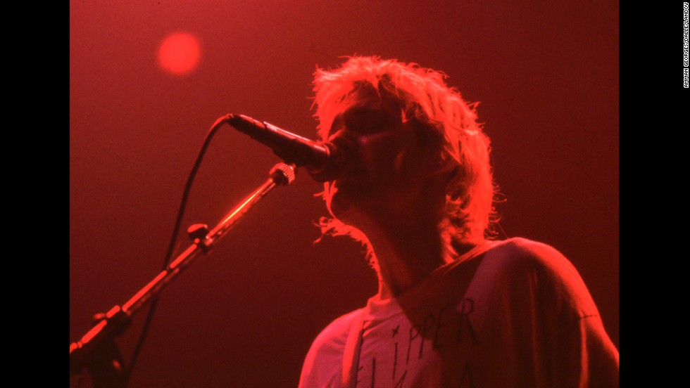 A photo of Kurt Cobain playing a show with Nirvana with a red light on him.