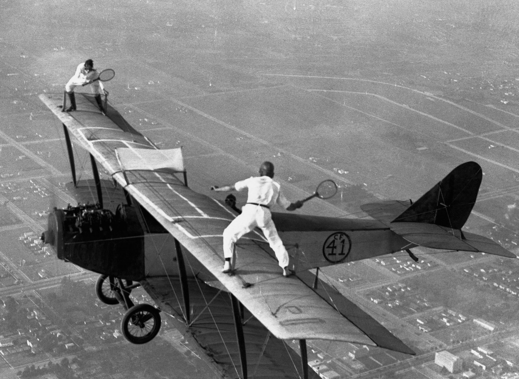Daredevils Gladys Roy and Ivan Unger Play Tennis In Sky, riding on the wings of a biplane as it flies over the city in November 1925.