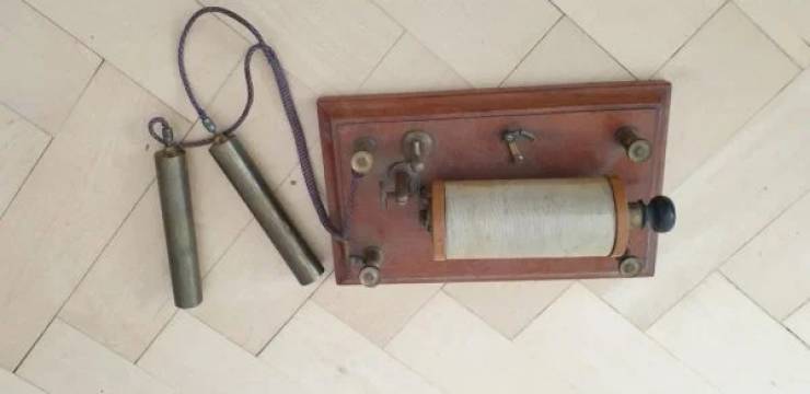 Wooden base plate with some type of coil o top, and two brass(?) Cylinders attached with a cord.Medical quackery shock therapy device.