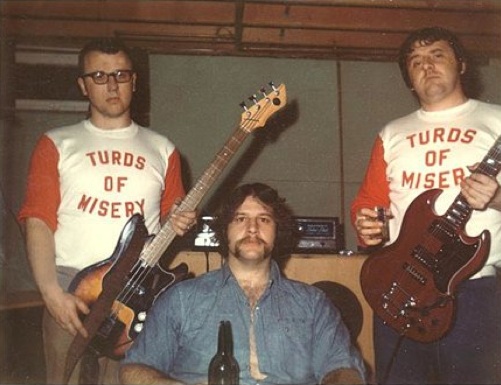 This was a real band. Turds of Misery played only 6 shows during their short existence. Based in a small town on the outskirts of Winnipeg, Manitoba, the 3-piece act quickly abandoned their first concept -- an Alan Parson Project cover band -- to focus on original tunes. The band included from left bassist Dave, drummer Gord, and guitarist Bagpipes