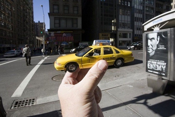 In These Streets - Is this a real New York City taxi in the streets of the Big Apple with a hand just imposed in the picture? Or is this just a toy version of a cab being held by an actual hand with a NYC street backdrop?