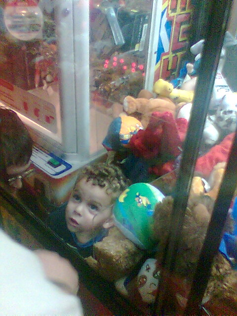 Kid trapped the claw machine. He climbed inside so that he could play with the toys.