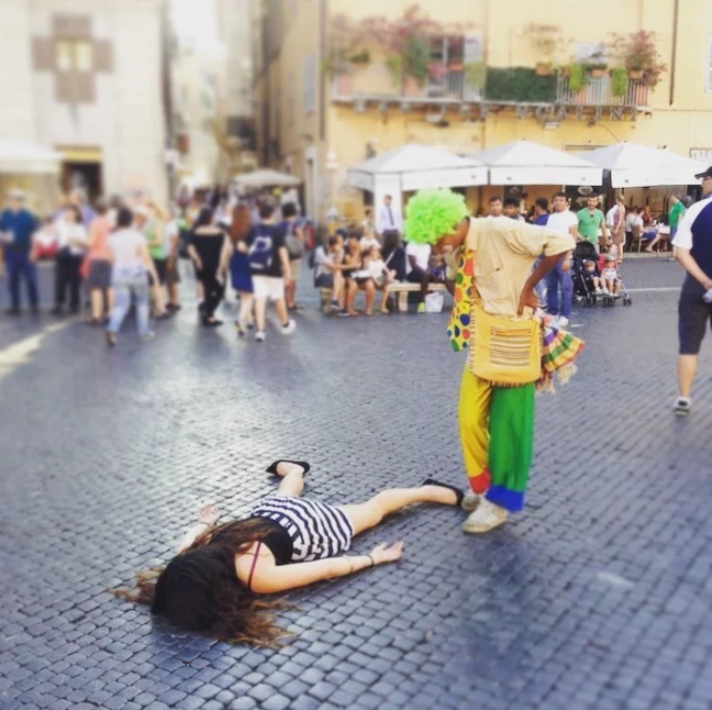 Artists are always pushing new boundaries to express themselves.   This woman felt posing dead at public places & famous landmarks would shift the focus away from her.  She may be half right.  It took a moment or two to find her in some of these, however most people in the photos are looking at her with total confusion.   Here she is on the Clown's Turf in Rome, Italy.