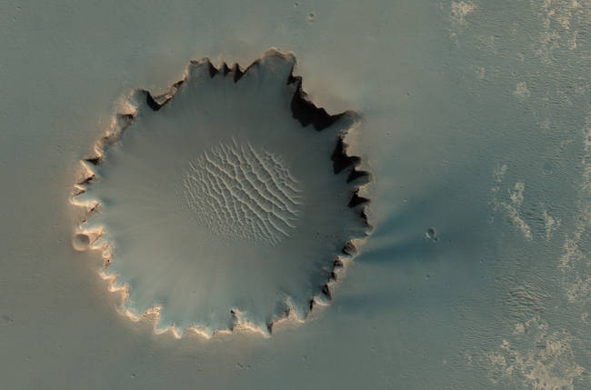 Victoria Crater at Meridiani Planum. The crater is approximately 800 meters about half a mile in diameter. Layered sedimentary rocks are exposed along the inner wall of the crater, and boulders that have fallen from the crater wall are visible on the crater floor. NASA's Mars rover Opportunity explored this crater and its walls in 2006. More, or see location on Google Mars.