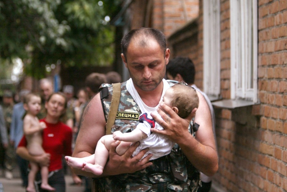 A Russian police officer carries a released baby from the school seized by heavily armed masked men and women
