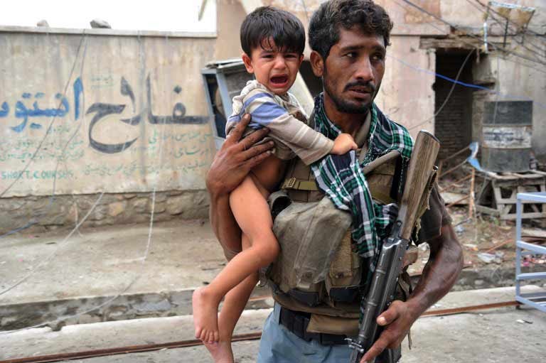 An Afghan soldier carries a crying child away from the scene of a recent explosion. Afghanistan War, c. 2001 - 2014