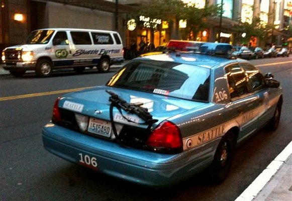 Seattle police leave a rifle laying on a squad car.  Several people noticed it and a bicyclist chased the cop down to tell him about it. 