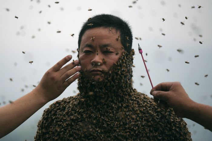 Assistants use burning incense and cigarettes to keep bees away from She Ping's face as his bee suit builds.