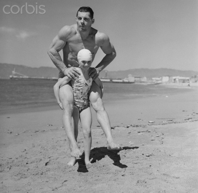 Female bodybuilder Patricia O’Keefe, who weighed only 64 pounds, gives a 200 pound man a piggyback ride. [1940]