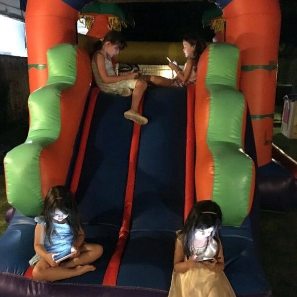 sad picture of kids playing with their glowing phones on an inflatable jumping castle slide