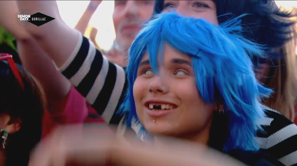 Woman in the crowd with blue hair, whited eyes, and missing front teeth.